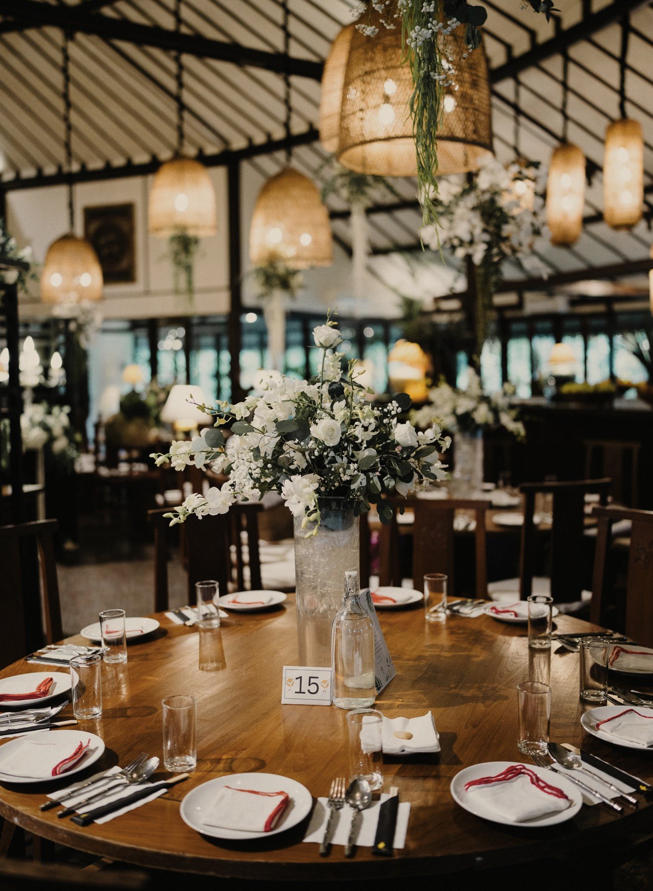 Round teak table set for a dinner under rattan lamps